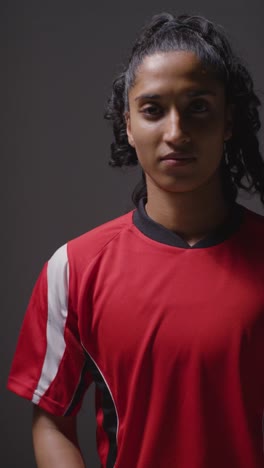 Vertical-Video-Studio-Shot-Of-Female-Footballer-Wearing-Club-Kit-Against-Grey-Background-Turning-Around